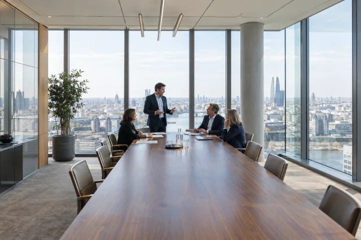 A supplier presenting to a procurement team of three at a long table in a high-rise office with a city view